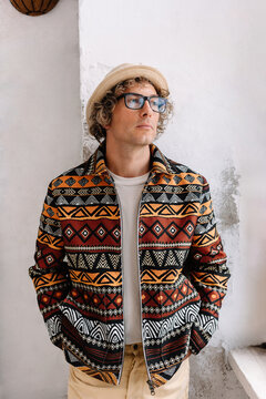 Man stands in unique patterned jacket and hat indoors
