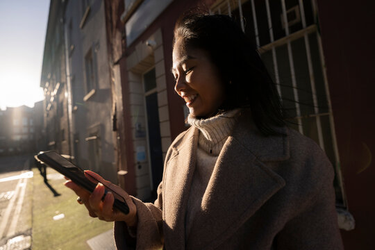 Happy Woman Checks Her Mobile Phone on a Winter Day in the City