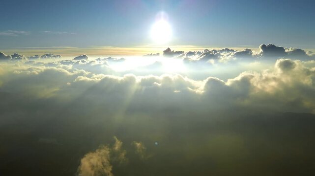 Aerial view of the bright sun shining over a sea of fluffy white clouds with sunbeams piercing through the hazy atmosphere in Indonesia.