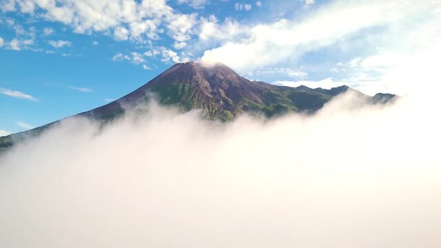 Aerial view of a drone flying through thick white clouds and dense mist with a glimpse of blue sky in Indonesia.