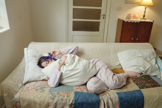 Person with colorful hair resting in the couch hugging a cushion 