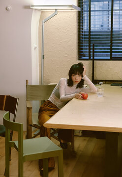 Asian fashionable woman is leaning lazily against a dining table 