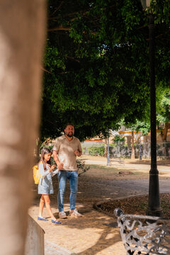 Father and daughter walking in sunny park after school 