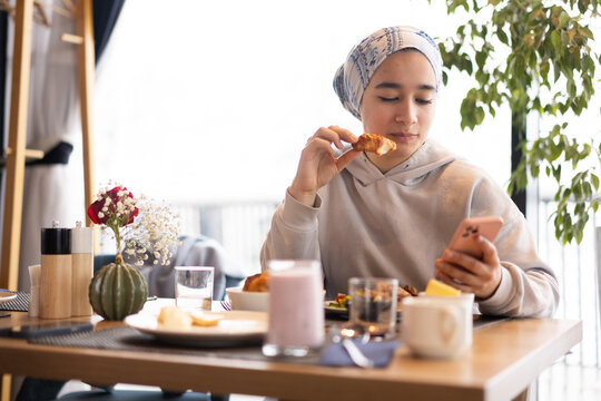 Muslim Woman Checking Smartphone While Eating in Restaurant