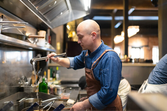Bald male chef pouring water on pan