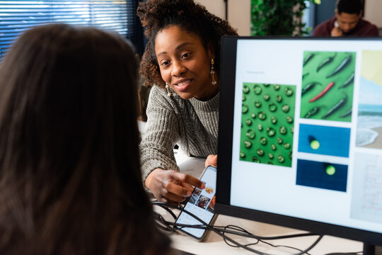 Woman showing photos on smartphone to colleague 
