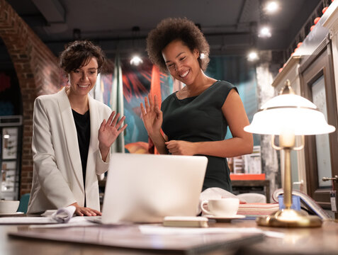 Cheerful multiracial female designers greeting online colleagues