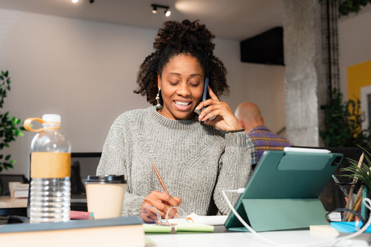 Cheerful woman talking to client via phone call from office 