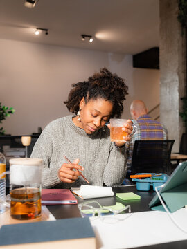 Thoughtful woman writing ideas in notepad at work 