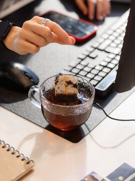 Person Brews Tea at Desk While Using Computer and Phone