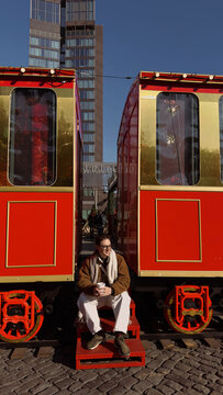 Winter scene with man sitting by two red train cars in city