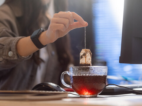 Woman dipping teabag in mug at office 