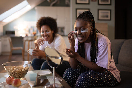 Black woman applying under eye patch near friend