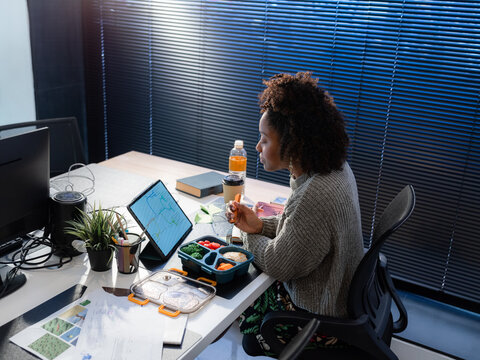 Woman Eating Lunch at Desk While Working in Modern Office