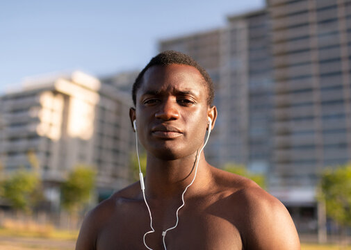 Handsome muscular Black sportsman with earphones outside