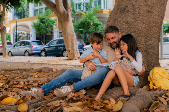 Man reading book to his kids in park 