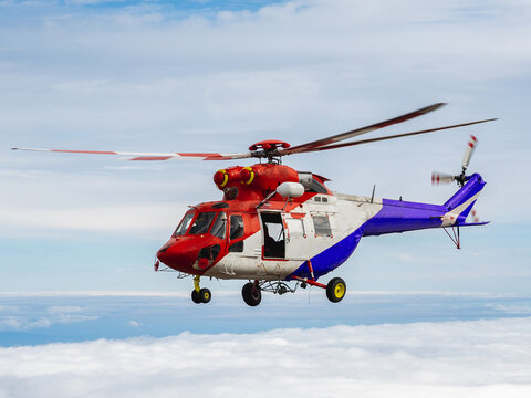 Red rescue helicopter flying above mountains and clouds.