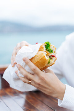 Hands holding sandwich with greens and fish by the sea