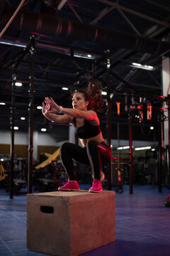 Powerful sportswoman jumping on gym box