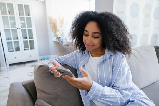 Young black woman using smartphone on sofa at living room at home