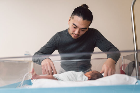 Father looking at newborn baby in hospital bassinet