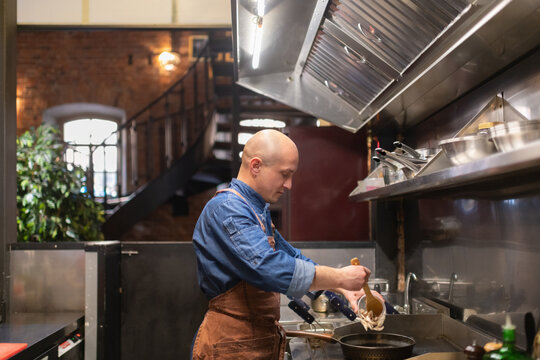 Bald male chef putting pasta on frying pan
