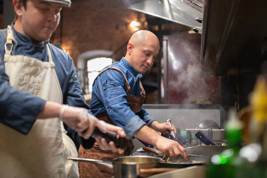 Male chef frying dish near colleague