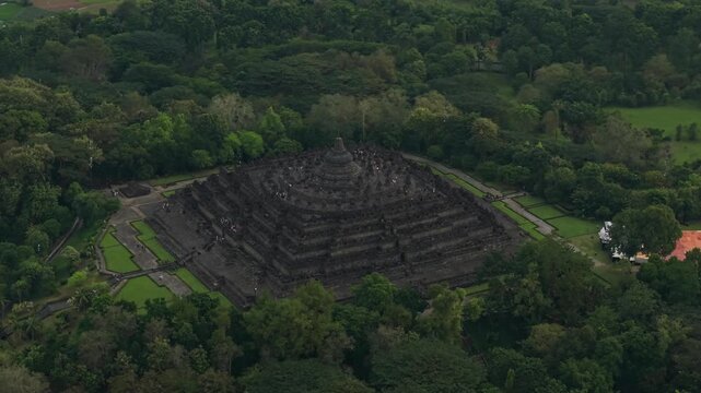 Aerial view of Borobudur Temple, a massive Buddhist monument surrounded by lush tropical forest and green lawns in Kecamatan Borobudur, Jawa Tengah, Indonesia.