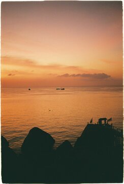 Sunset view over calm sea with boats at a distance and rocks
