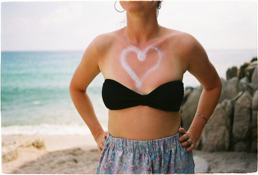 Woman with heart shape sunscreen on skin stands on the beach