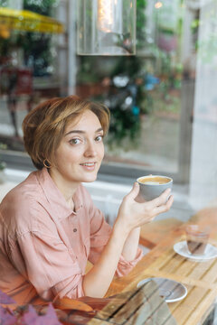 Woman holding coffee cup at window table 