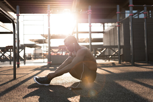 Sporty young male athlete tying laces during break between exercises