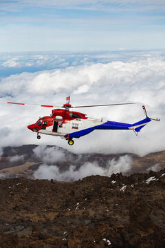 Red rescue helicopter flying above mountains and clouds.