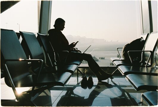 Person sits in airport terminal while using laptop and phone