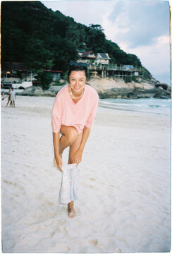 Woman standing on sandy beach pulling up shorts near ocean