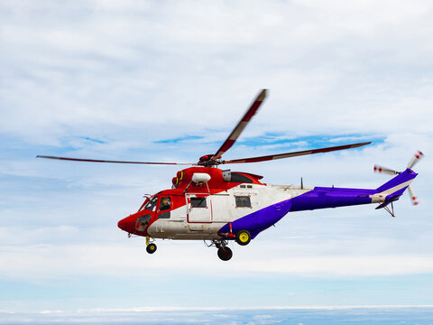 Red rescue helicopter flying above mountains and clouds.
