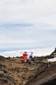Red rescue helicopter flying above mountains and clouds.