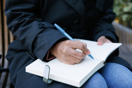 Cropped black businesswoman writing in notebook on bench outdoors