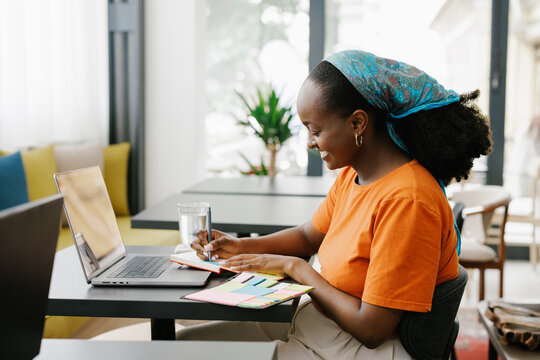 Woman Writes Notes While Working on Laptop in Cafe