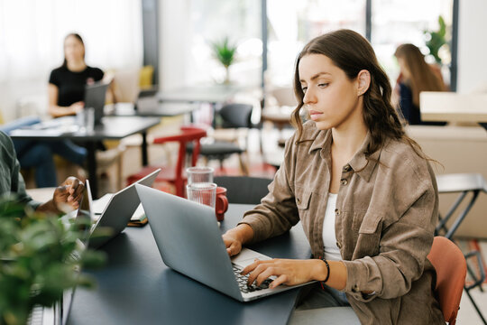 Young Woman Working on Laptop in a Busy Cafe During the Day