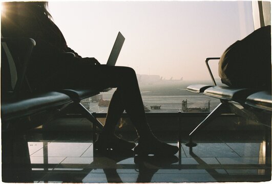 Person sits at airport terminal with laptop during sunset