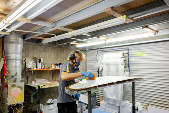 Worker laminating surfboard in glassing room