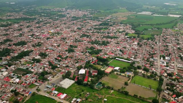 Aerial view of the town of Tuxpan featuring red rooftops, green fields, and misty mountains under a cloudy sky in Tuxpan, Jalisco, Mexico.