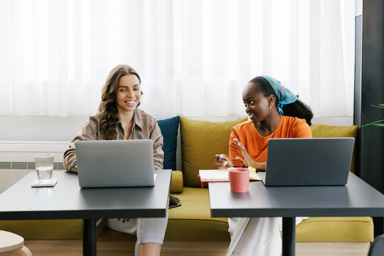 Two Women Working at a Table in a Bright Cafe Using Laptop