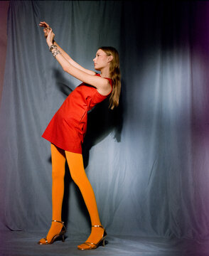 Woman in Red Mini Dress and Yellow Tights Leaning with Raised Arms