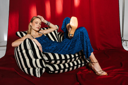 Relaxed Editorial Pose in Striped Armchair with Red Studio Drapery