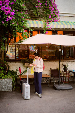 Traveler Checking Phone Near Cafe With Flowers in the Background