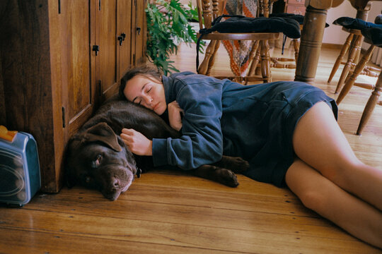 A woman naps on a wooden floor resting a head on a dog 