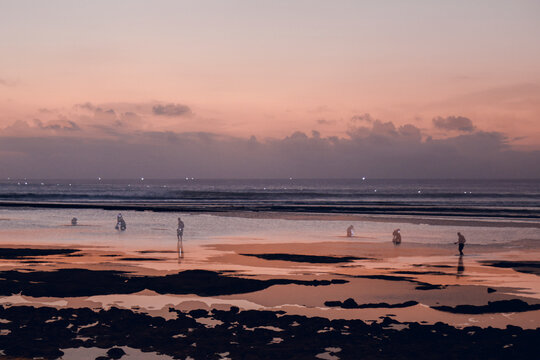 People searching tidal pools on beach at sunset in Bingin