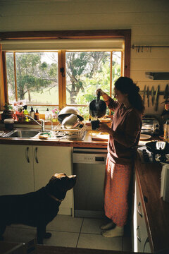 Woman pours water from the kettle with the dog in the kitchen 